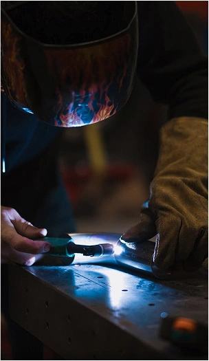 Welder performing precision welding with protective gloves and mask.