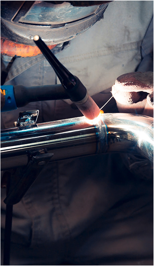 Close-up of TIG welding on a metal pipe using a torch and filler rod.