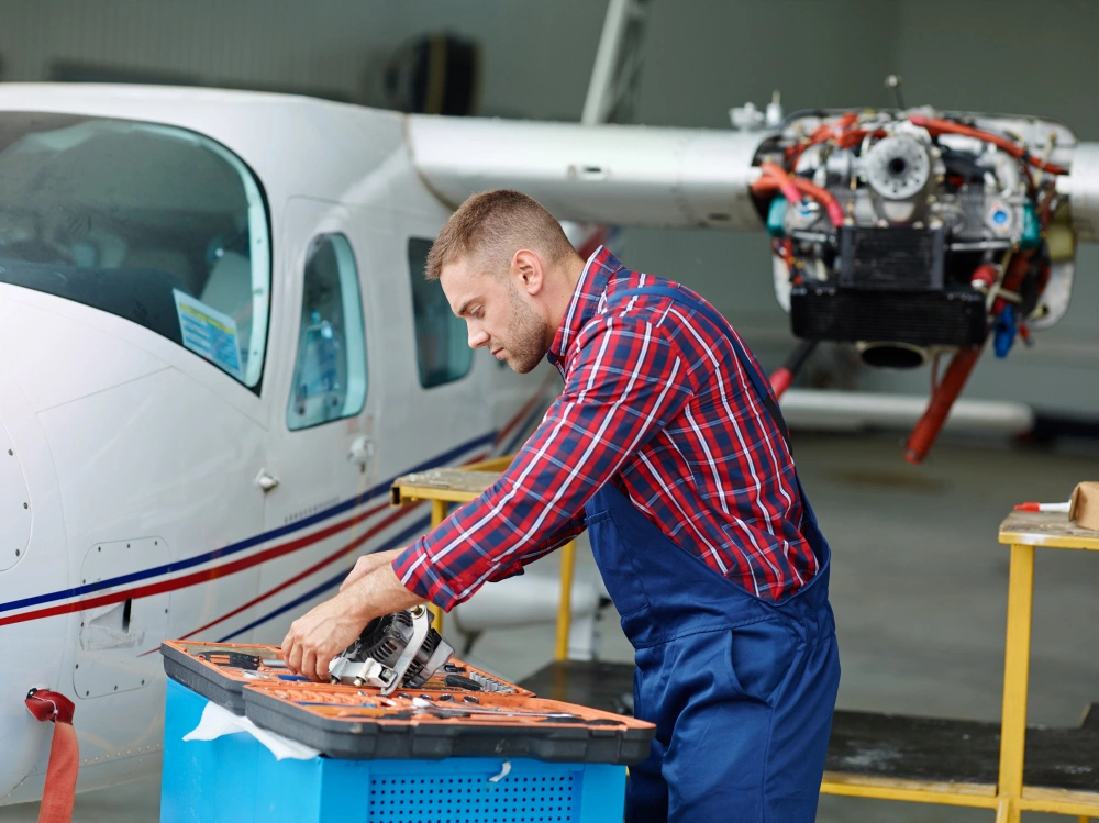 Aircraft mechanic working on tools beside a small airplane inside a hangar.