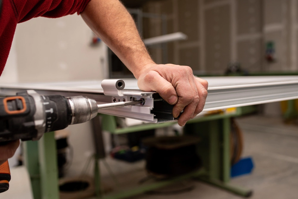 Worker using a power drill to assemble or install an aluminum frame.