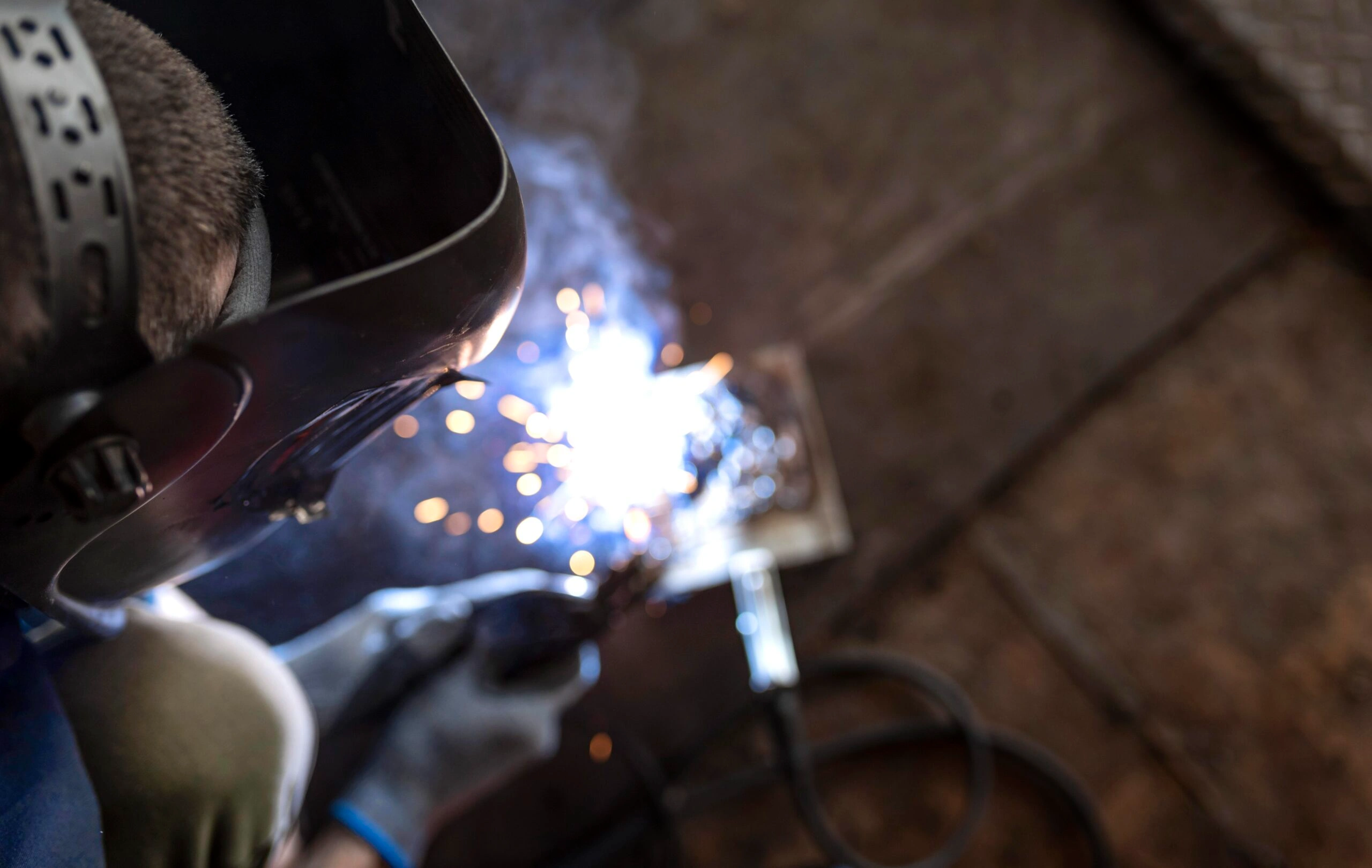 Welder wearing protective helmet performing metal fabrication with bright sparks.